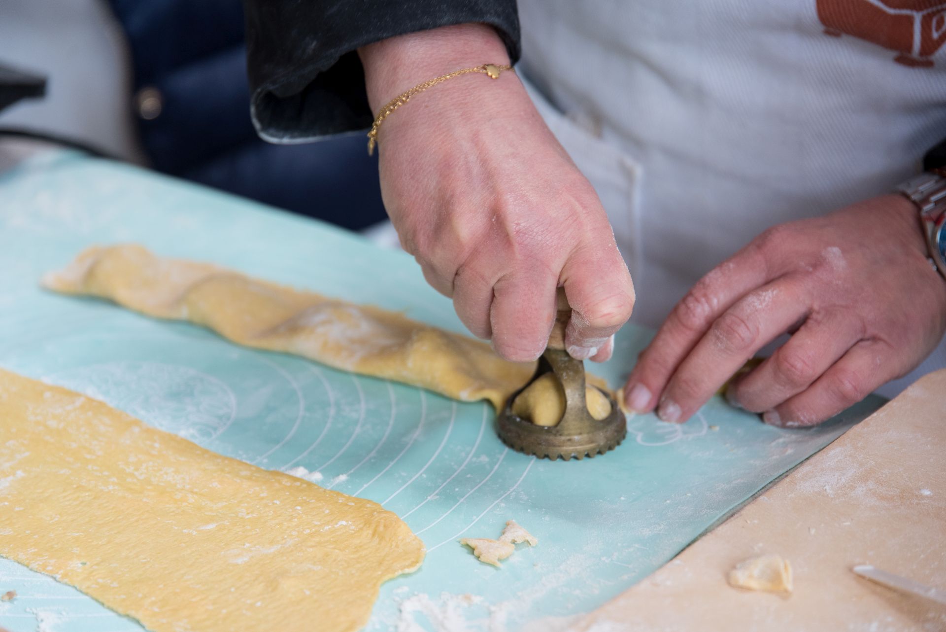 primo piano di due mani che ritagliano un tordello da una striscia di pasta su un tavolo infarinato